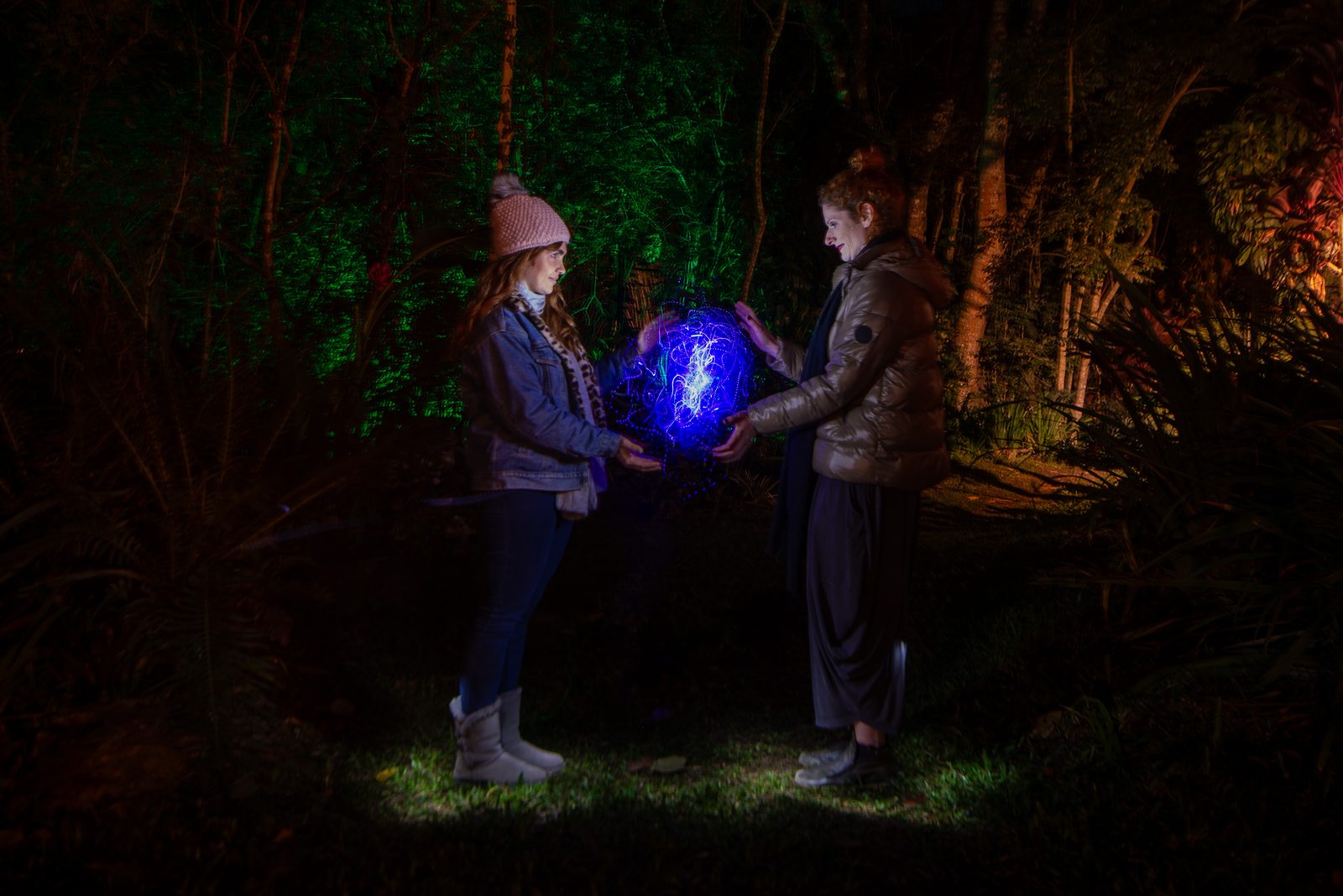 Duas pessoas segurando uma esfera de luz azul no escuro, durante uma noite de light painting