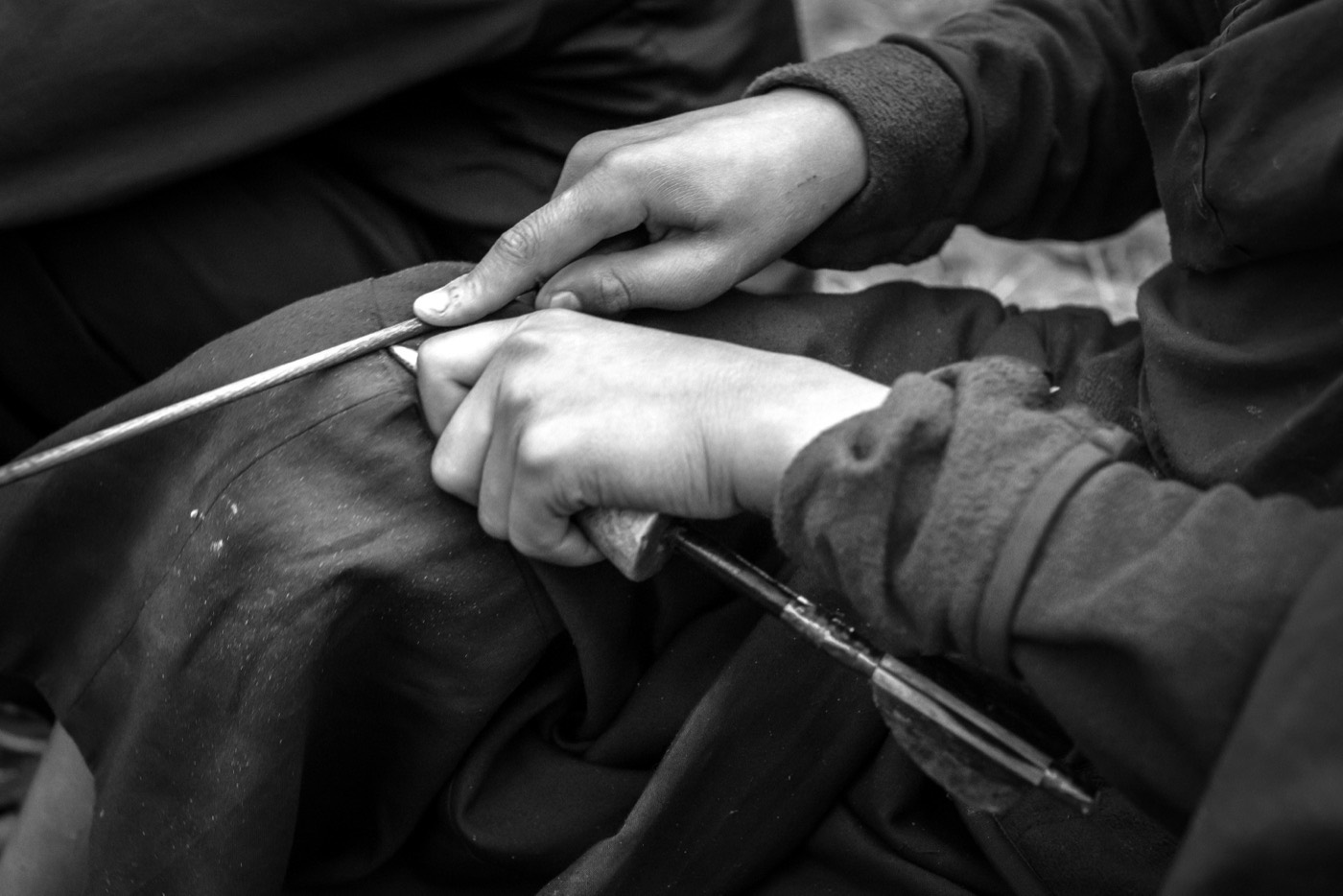 Duas mãos trabalhando com uma agulha sobre tecido, em preto e branco